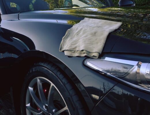Panno in microfibra appoggiato sul cofano nero lucido di un'auto, dettaglio del faro e del pneumatico. Servizio di autolavaggio professionale.