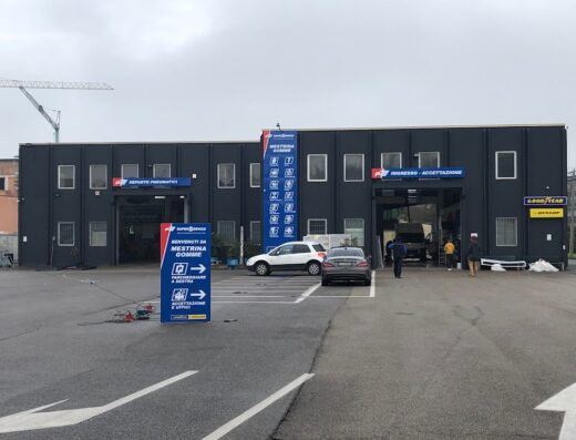Mestrina Gomme Centro SuperService Centro Revisioni: Facciata dell'officina con insegne 'Reparto Pneumatici', 'Ingresso Accettazione', Goodyear e Dunlop, auto parcheggiate.