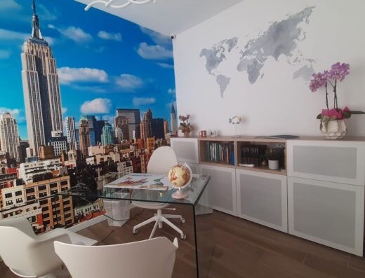 Ufficio di agenzia viaggi MG Travel con scrivania in vetro, mappamondo, parete con skyline di New York e cartina geografica