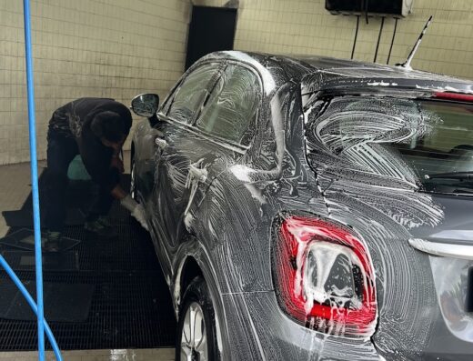 Mister Lavaggio lava un'auto grigia, insaponandola a mano in un autolavaggio. Servizio di pulizia professionale per auto.