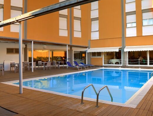 Piscina esterna dell'Hotel Mistral 2 con lettini prendisole, tavoli e sedie per il relax. Ambiente accogliente per un soggiorno confortevole.