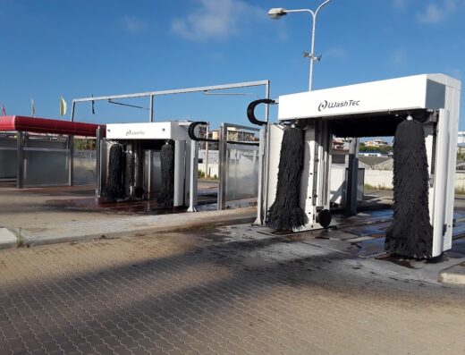 Two WashTec automatic car wash bays with large black brushes under a blue sky at a mixing park.