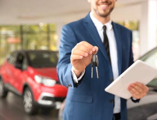 Uomo in giacca blu che offre le chiavi di un'auto rossa e nera per il noleggio a lungo termine di Mobility Rent Srl a Torino