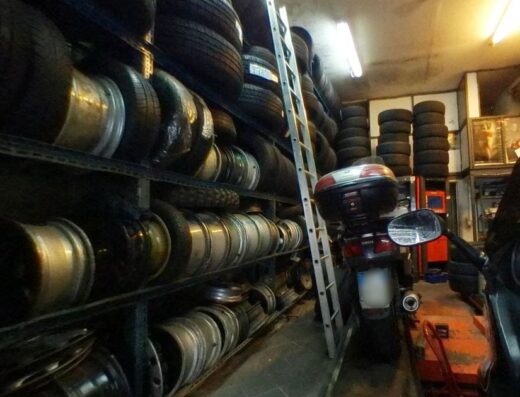 Magazzino di Moltomoli Massimo con scaffali pieni di pneumatici e cerchi per moto, scala appoggiata e moto con bauletto visibile.