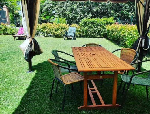 Tavolo da pranzo in legno con sedie in vimini e metallo sotto un gazebo in un giardino verde a Monferrato Bed&Bike.