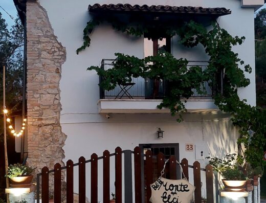 Monte degli Elci B&B: Facciata esterna della struttura ricettiva con cancello in legno, balcone fiorito e insegna "Monte Elci". Ideale per viaggi in moto e relax.
