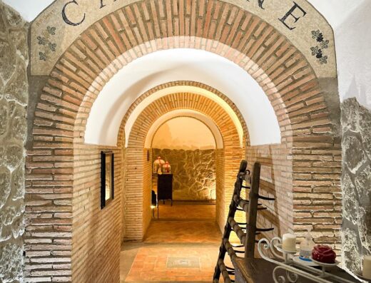 Interno delle cantine dell'agriturismo Monte Due Torri, con arcate in mattoni, pavimento in cotto e scritta "Cantine" sopra l'ingresso.