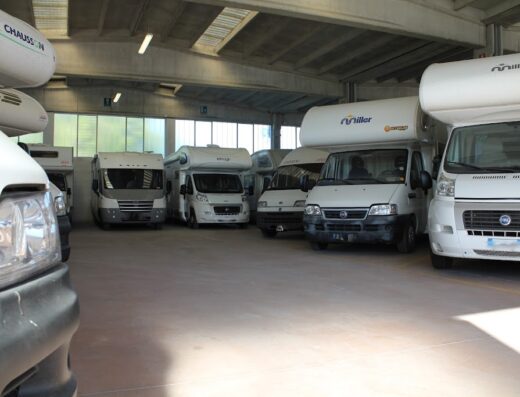 Parcheggio interno con diversi camper bianchi di varie marche e modelli, ideali per viaggi e vacanze on the road, visibili alcuni marchi come Miller e Chaussen.