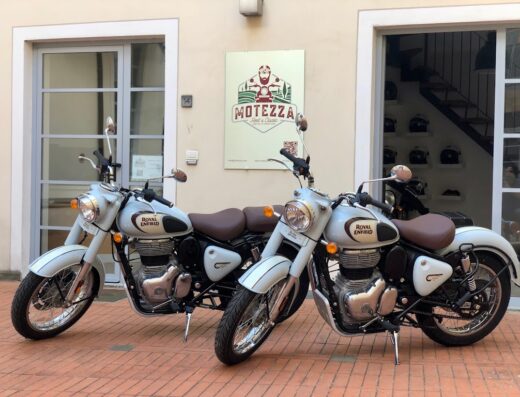 Due motociclette Royal Enfield Classic bianche parcheggiate di fronte a MOTEZZA Rent A Classic, perfette per un'avventura di viaggio su due ruote.
