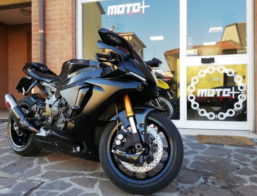 Moto nera sportiva parcheggiata di fronte a un negozio Moto+; dettaglio degli accessori e del design della moto.