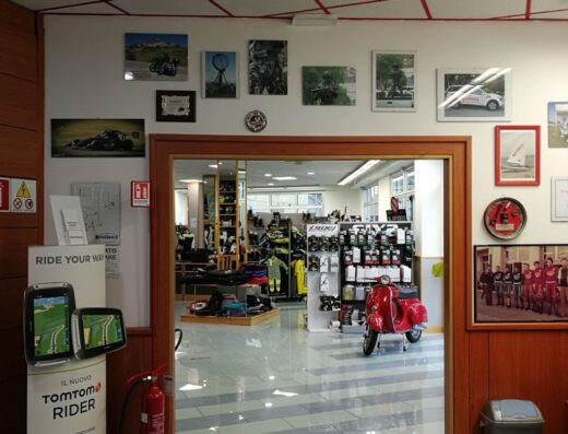 Interno del negozio Moto Charlie abbigliamento con esposizione di accessori moto, caschi, abbigliamento tecnico e una Vespa rossa