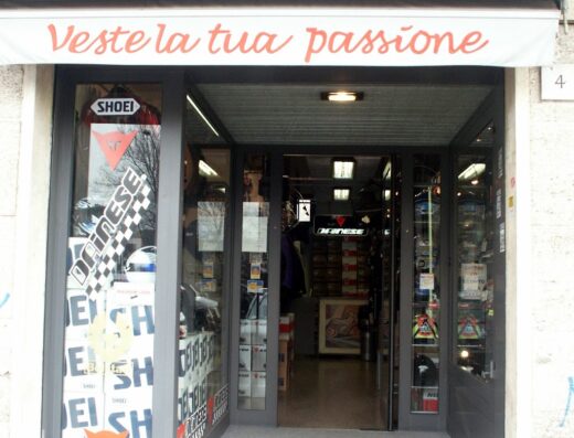 Ingresso del negozio Moto City, specializzato in caschi e abbigliamento da moto. Vetrina con adesivi Shoei e Dainese, ampia scelta di accessori e protezioni per motociclisti.