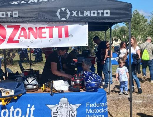 Stand del Moto Club Michele Mammola Racing Team ASD con caschi moto, accessori e logo Federazione Motociclistica Italiana (FMI).