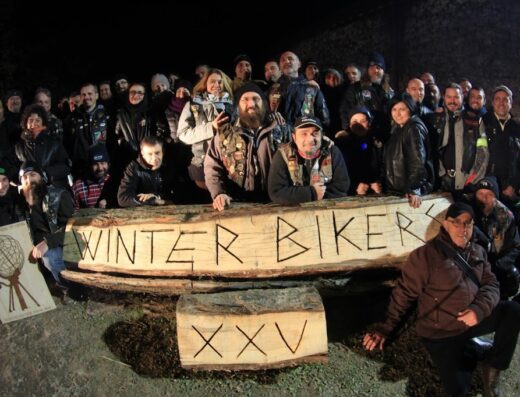 Gruppo di motociclisti del Moto Club Winter Bikers posa dietro un cartello di legno con la scritta "Winter Bikers XXV", abbigliamento da moto invernale
