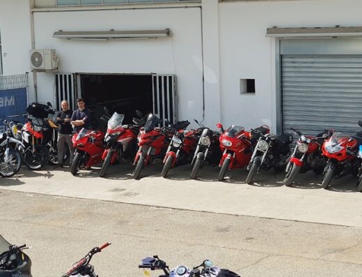 Gruppo di moto da competizione parcheggiate di fronte a un'officina, con meccanici che le ispezionano, pronte per la gara o il servizio di manutenzione