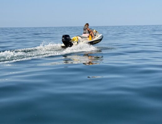 Una donna guida una moto d'acqua Majellando sul mare calmo in una giornata di sole. L'acqua blu è increspata dal movimento della moto d'acqua.