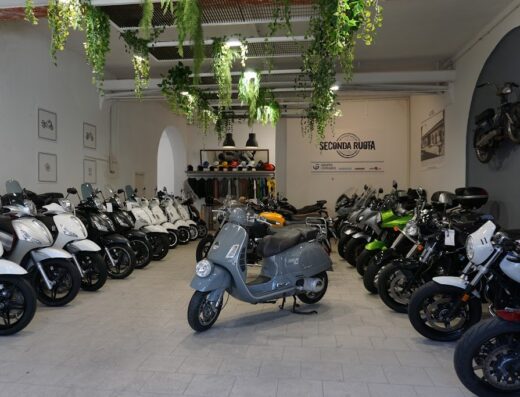 Interno di Seconda Ruota a Lucca, concessionario di moto e scooter usati: esposizione di scooter Vespa grigio in primo piano e moto di diversi modelli sullo sfondo.