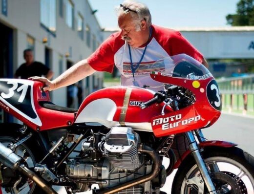 Un uomo esamina una moto Moto Guzzi d'epoca rossa e bianca con il numero 3 e il logo Moto Europa su un circuito.