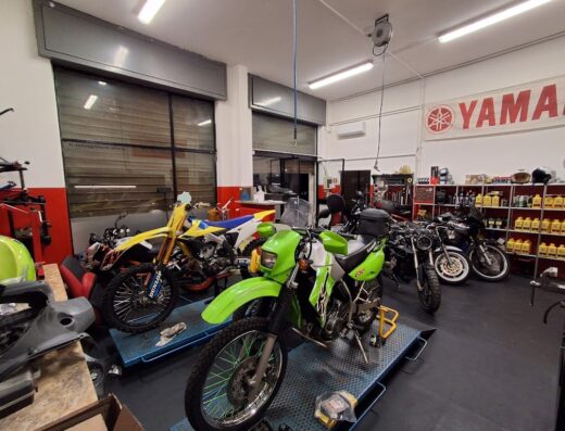Interno di officina meccanica di Patuzzi Emanuele con diverse moto, tra cui una Kawasaki verde, una moto da cross gialla e altre moto customizzate e accessori.