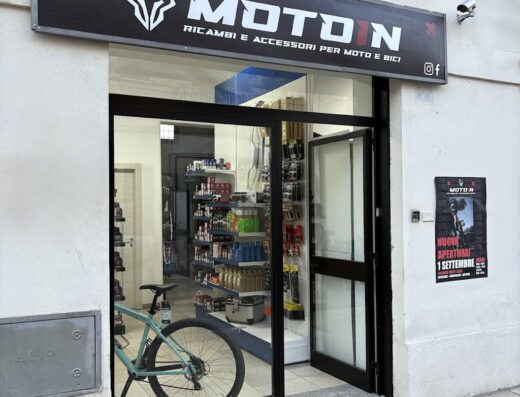 Ingresso del negozio Moto IN, specializzato in ricambi e accessori per moto e bici. In vetrina si intravede una bicicletta. Servizi e marketplace per motociclisti.