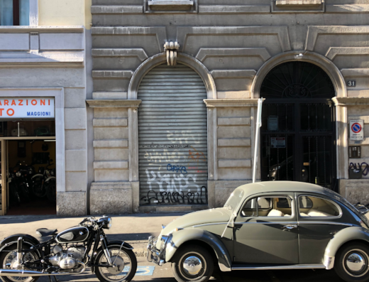 Moto Maggioni: Officina di riparazione moto d'epoca a Milano, con una BMW classica parcheggiata di fronte e un Maggiolino Volkswagen grigio.