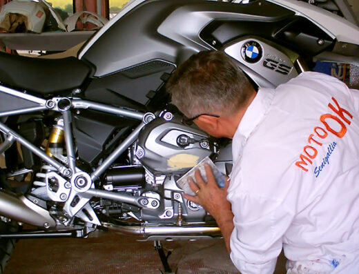 Tecnico di Moto Ok Senigallia che esegue la manutenzione su una moto BMW GS, riparando la carrozzeria. Servizi di riparazione moto e accessori.
