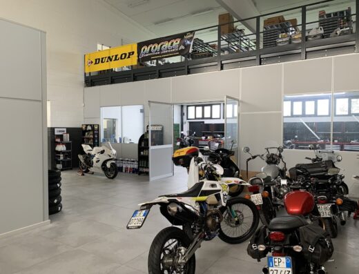 Interno dell'officina Moto Quadri Simone con diverse motociclette in esposizione e riparazione, pneumatici e scaffali di accessori.