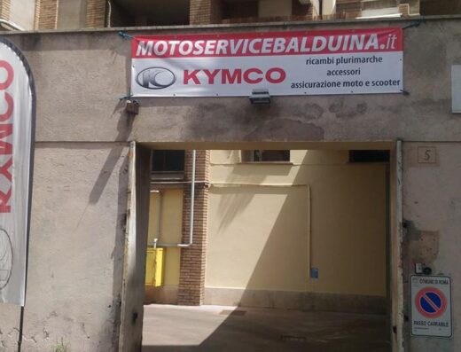 Ingresso di Moto Service Balduina, officina e concessionaria Kymco a Roma, con insegna "MOTOSERVICEBALDUINA.it" che offre ricambi, accessori e assicurazione moto e scooter.