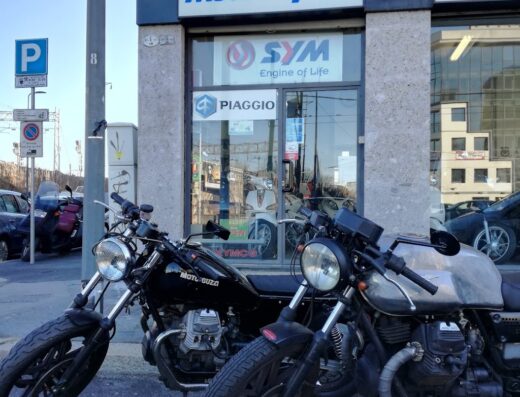 Moto e Sport: concessionario moto con due motociclette Moto Guzzi parcheggiate di fronte, con insegne SYM, Piaggio e Kymco.