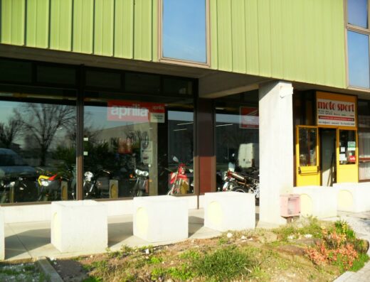Moto Sport dei F.lli Ciot- Motosport Factory Lab: esterno del negozio con vetrine che espongono moto Aprilia e Honda. Entrata gialla.
