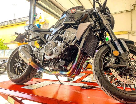 Moto Tech: Black Honda motorcycle with aftermarket SC Project exhaust system on a red hydraulic lift in a garage, showcasing motorcycle customization and service.