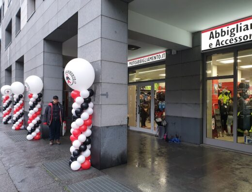 Ingresso del negozio di motoabbigliamento e accessori con decorazioni di palloncini bianchi, rossi e neri e insegna luminosa.