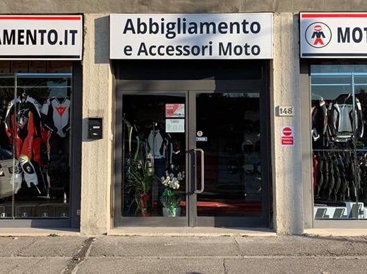 Foto della facciata di un negozio di motoabbigliamento e accessori moto, con vetrine che espongono tute, giacche e pantaloni per motociclisti.