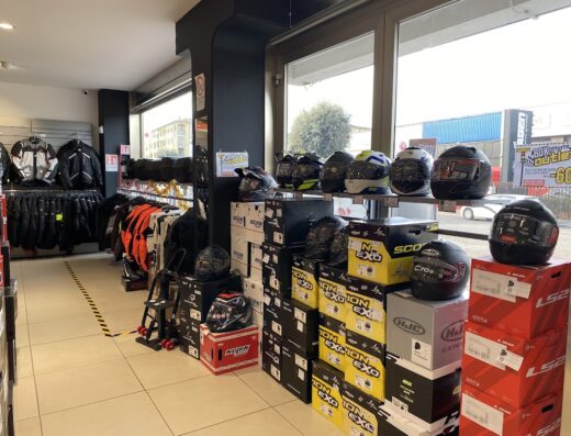 Interno di negozio di motoabbigliamento con esposizione di caschi da moto di diverse marche come Nolan, HJC e LS2, giacche tecniche e accessori per motociclisti