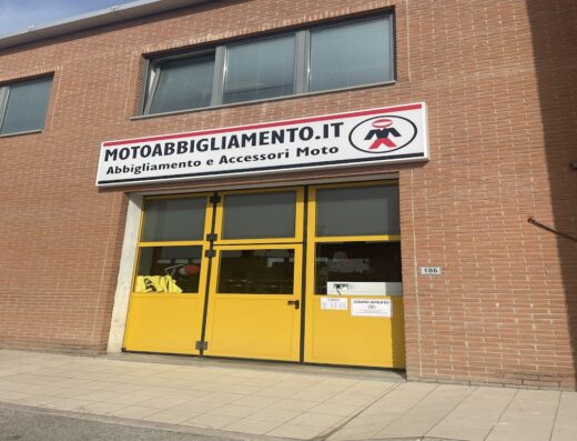 Foto del negozio Motoabbigliamento.it con insegna ben visibile, specializzato in abbigliamento e accessori moto. Ingresso giallo.