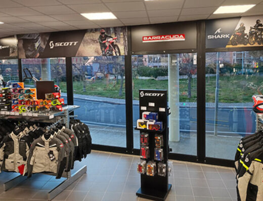 Interno di negozio di motoabbigliamento con giacche, caschi, e occhiali da moto in esposizione. Presenti i marchi Scott, Barracuda e Shark.
