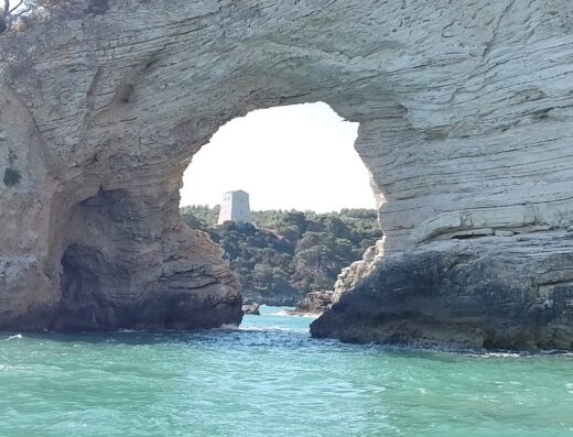 Arco di roccia sul mare a Vieste, con una torre storica sullo sfondo, visibile durante un'escursione in motobarca.