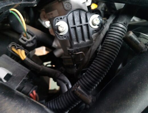 Dettaglio del motore di una moto con particolare attenzione ai cablaggi, connettori e un componente BMW fissato con viti, ideale per motocarrozzeria e riparazioni moto.