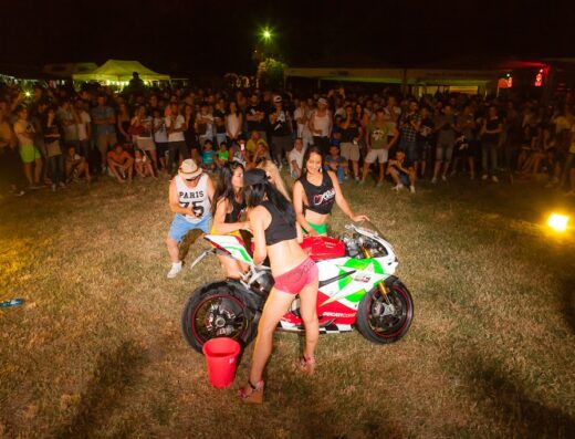 Tre ragazze lavano una moto Ducati in un evento del Motoclub Matti di Corinaldo, circondate da una folla di persone.