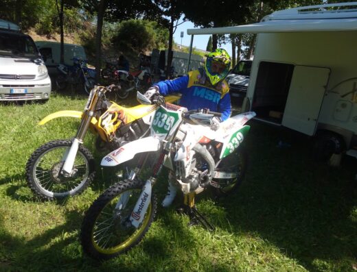 Un pilota di motocross in posa sulla sua moto Suzuki numero 339 durante un evento del Motoclub Romans, accanto a un camper e altre moto.