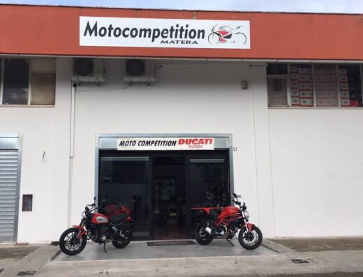 Motocompetition Matera: officina e negozio specializzato Ducati. Due moto Ducati rosse parcheggiate davanti all'ingresso del negozio.