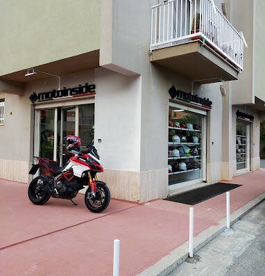 Motoinside: Ducati Multistrada parked outside a motorcycle accessories and marketplace shop. Helmets visible in the shop window.