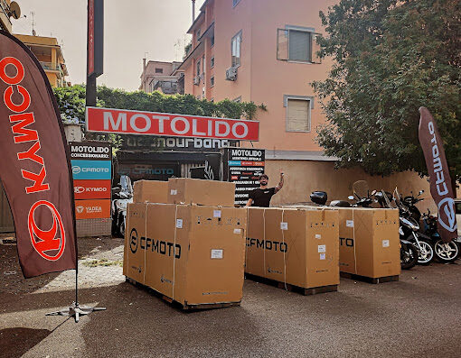 Concessionaria MOTOLIDO Roma Appia: moto KYMCO, CFMOTO e VOGE nuove in arrivo, con cartoni e personale. Vetrina moto e bandiere dei marchi.