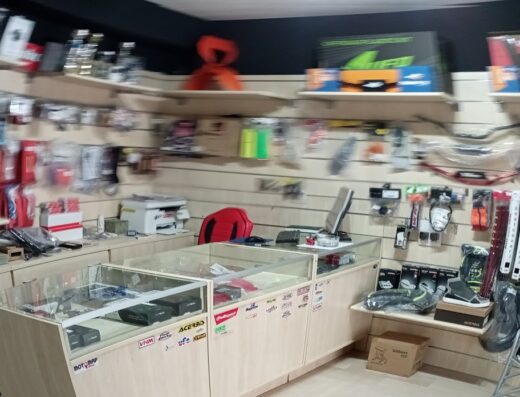 Interno del negozio Motomap SAS con esposizione di accessori e ricambi moto. Caschi, stivali, manubri e altri prodotti per motociclisti visibili sugli scaffali e vetrine.