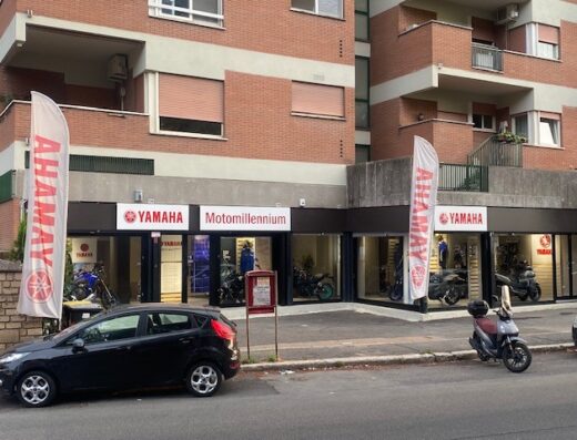 Motomillennium Yamaha Roma Eur: concessionaria Yamaha con moto esposte, scooter parcheggiato e auto nera di fronte.