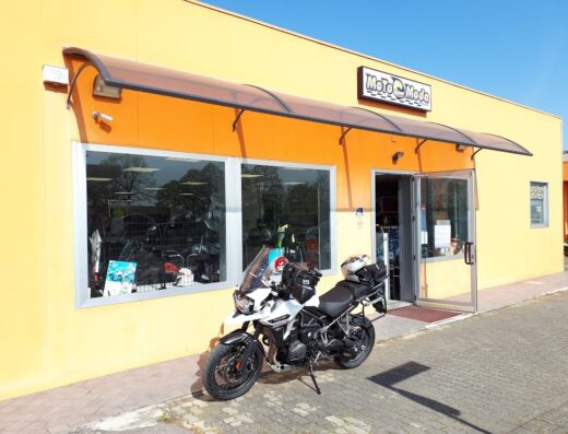 Motocicletta da turismo parcheggiata di fronte al negozio Motomoda, specializzato in accessori e abbigliamento per motociclisti e viaggi in moto.