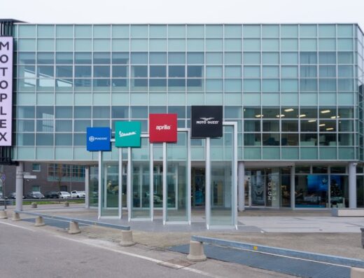 Motoplex building exterior featuring Piaggio, Vespa, Aprilia, and Moto Guzzi brand signage, showcasing a marketplace for motorcycles and related services.