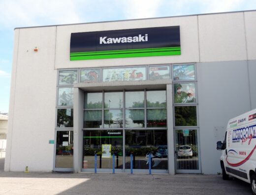 Facciata di Motopoint Racing S.r.l., concessionaria Kawasaki, con vetrine che espongono immagini di moto e accessori. Furgone aziendale parcheggiato di lato.