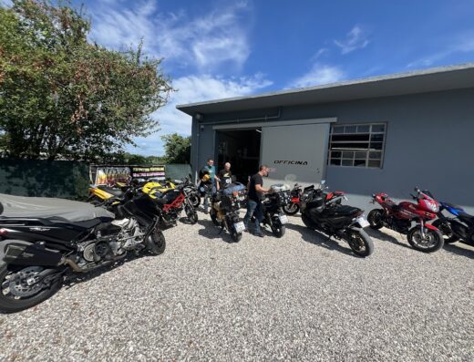 Gruppo di motociclisti davanti all'officina MOTOPOWER UDINE con diverse moto parcheggiate, tra cui modelli Ducati e Yamaha TMax, in attesa di assistenza e riparazioni.
