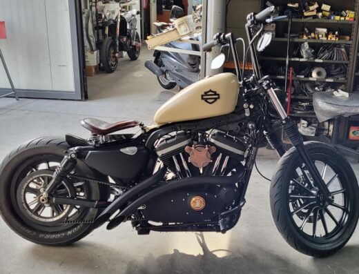 Moto Harley-Davidson customizzata in garage: serbatoio beige, sella in cuoio, manubrio alto. Accessori e modifiche per appassionati di moto e viaggi.